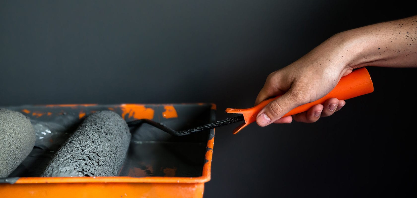 Close up of hand holding paint roller in paint tray, Grey wall background